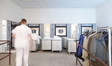 Busy hospital laundry room with staff operating large industrial washing machines