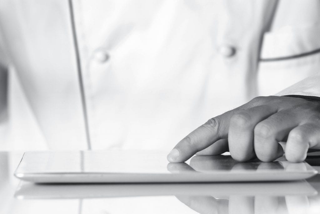 Close-up of a chef's hand browsing on a digital tablet in a kitchen setting