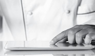 Close-up of a chef's hand browsing on a digital tablet in a kitchen setting