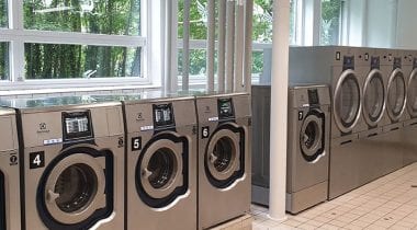 Row of Electrolux commercial washing machines by a window in a bright laundry facility
