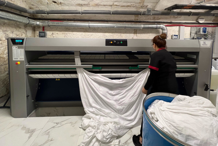 Staff member ironing large linens using Electrolux Professional flatwork ironer in hotel laundry facility