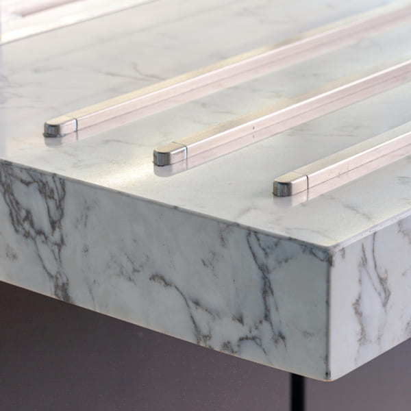 Close-up of a marble countertop edge with integrated stainless steel rods running horizontally across the surface, highlighting the sleek and modern kitchen design.