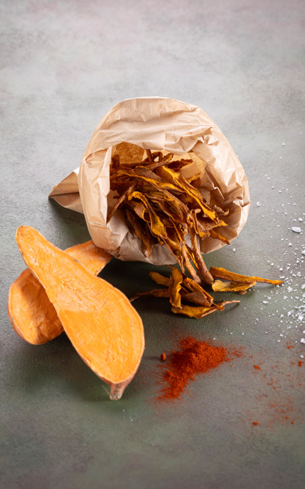 Zero waste sweet potato peel chips in a paper bag with raw potatoes and paprika powder