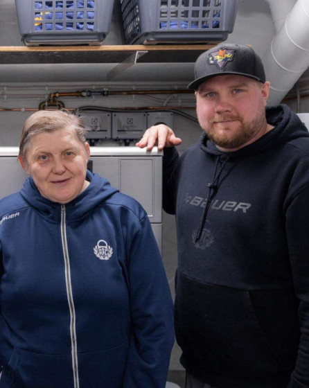 Two staff members standing in front of Electrolux Professional laundry equipment at sports facility supporting ice hockey team